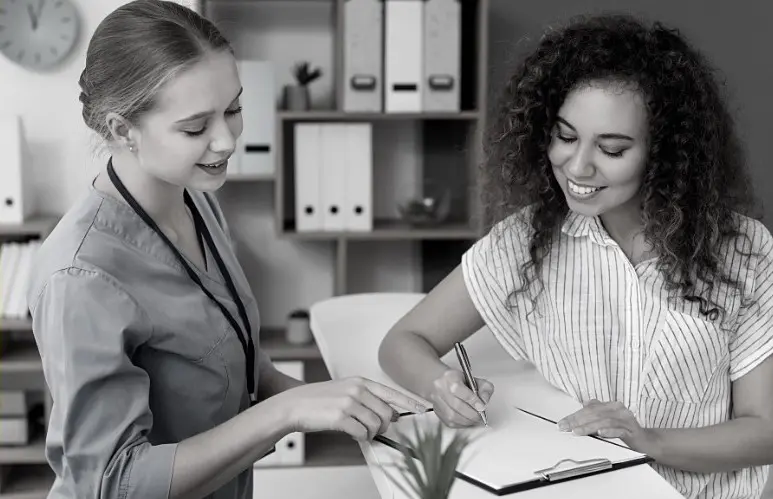 Two women are smiling while one of them is writing.